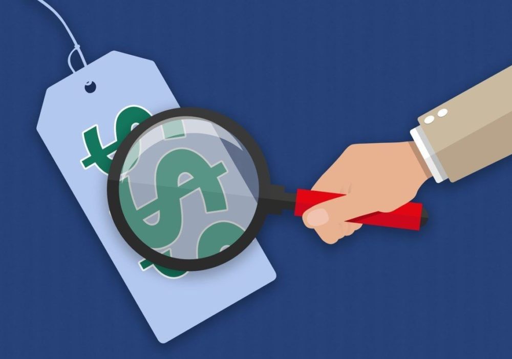 “An illustration of a hand holding a magnifying glass examining a price tag with dollar signs, representing cost analysis or price evaluation.”