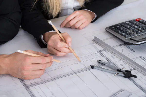 “Architects or engineers reviewing and marking building floor plans with technical drawing tools, calculators, and scale rulers on a construction blueprint.”