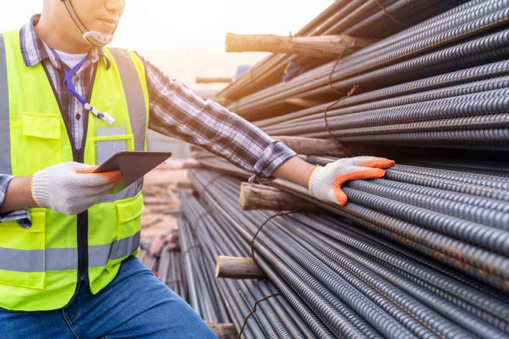 “Construction site worker inspecting steel reinforcement bars while using a digital tablet for quality control..